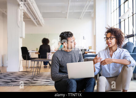 les gens d'affaires parlent tout en utilisant un ordinateur portable au bureau Banque D'Images