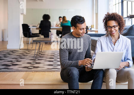 les gens d'affaires utilisant un ordinateur portable pendant que des collègues travaillent au bureau Banque D'Images