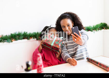 Heureuse mère et fille prenant selfie avec cadeau de noël à la maison Banque D'Images