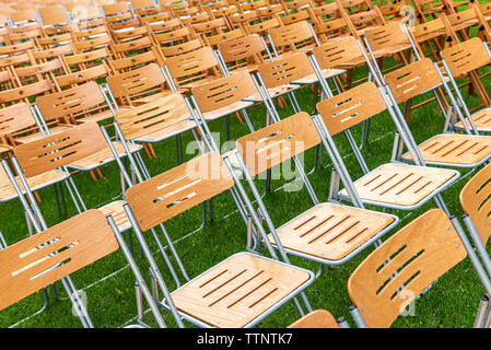 Beaucoup de chaises en bois se tiennent à l'extérieur dans le parc sous la pluie. Empty auditorium, l'herbe verte, des arbres et des chaises avec des gouttes d'eau. Banque D'Images