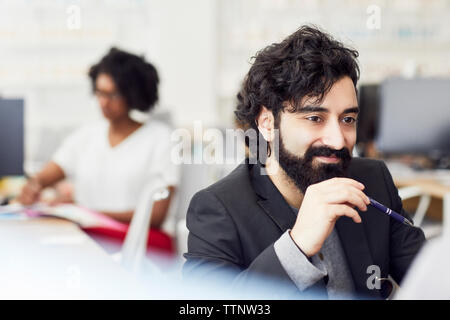 Thoughtful businessman looking away avec collègue assis en arrière-plan Banque D'Images
