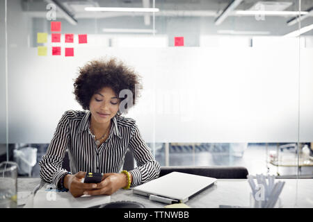 femme d'affaires utilisant le téléphone intelligent tout en étant assis dans le bureau Banque D'Images