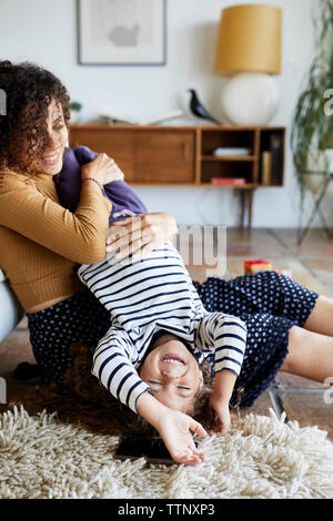 Happy mother holding daughter upside down while sitting on floor at home Banque D'Images
