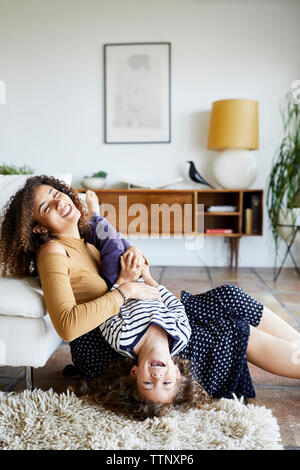Happy mother holding daughter upside down while sitting on sofa at home par étage Banque D'Images