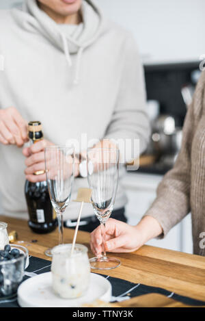 Portrait de l'homme ouvrant en position debout avec Prosecco copine à table dans la cuisine Banque D'Images