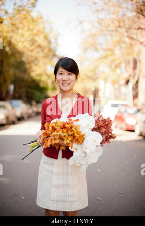 Portrait of smiling holding propriétaire bouquets en se tenant sur le road Banque D'Images