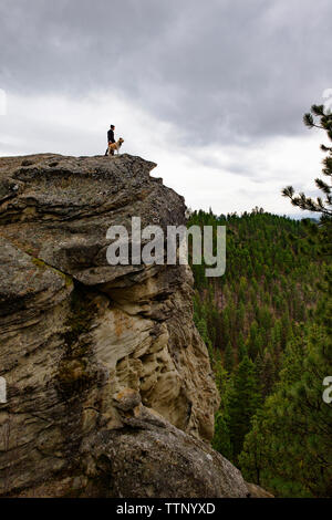 Low angle view of man and dog standing on cliff contre ciel nuageux Banque D'Images