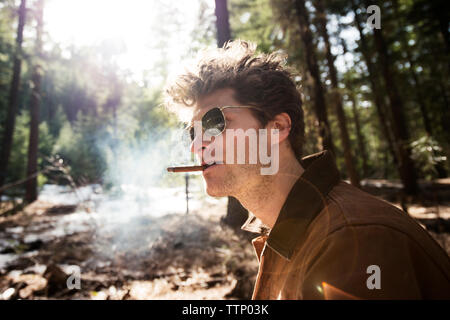 Side view of man smoking cigar in forest Banque D'Images