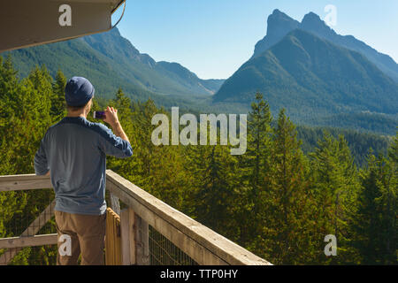 Vue arrière de l'homme photographie par le biais de smart phone en étant debout à heybrook lookout tower contre montagne Banque D'Images