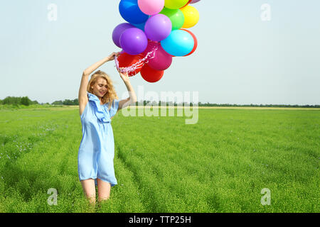 Femme heureuse avec des ballons colorés dans le champ sur fond de ciel bleu Banque D'Images