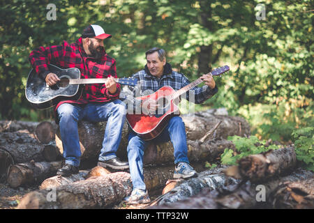Amis joueurs de guitare tout en étant assis sur des rondins dans la forêt Banque D'Images