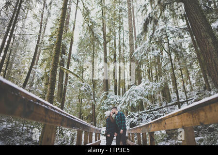 Couple en étant debout sur la passerelle au milieu d'arbres en forêt à Lynn Canyon Park en hiver Banque D'Images