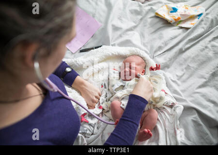 Portrait de sage-femme examining newborn baby girl with stethoscope on bed at home Banque D'Images