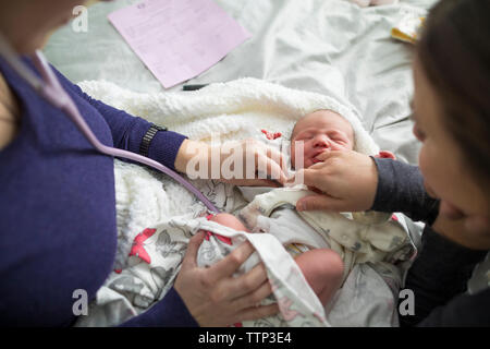 Portrait de sage-femme examining newborn baby girl par woman on bed at home Banque D'Images