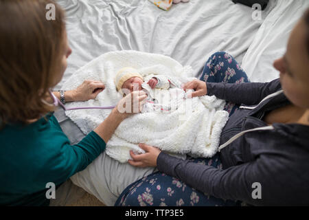 Portrait de sage-femme examining newborn baby girl alors que mère assis sur le lit à la maison Banque D'Images