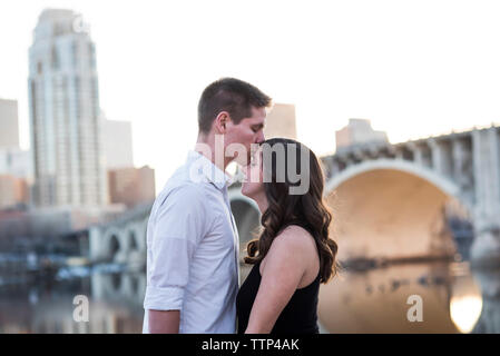 Mari, baiser sur le front de femme enceinte en position debout par river contre ciel clair en ville Banque D'Images