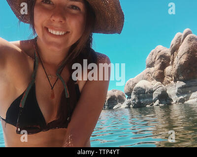 Portrait of smiling woman wearing bikini en nageant dans le lac contre le ciel bleu clair au cours de journée ensoleillée Banque D'Images