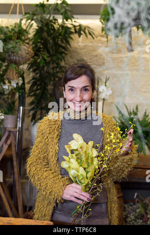 Portrait of smiling senior woman holding fleurs jaunes à flowershop Banque D'Images
