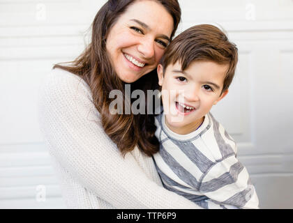 Portrait of happy mother carrying son debout contre le mur dans la cour Banque D'Images