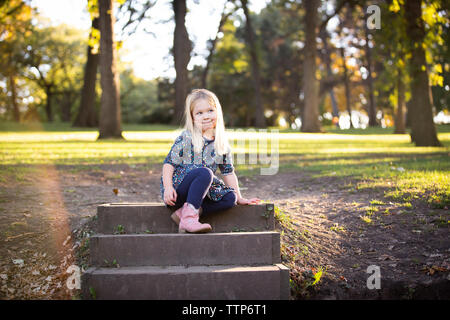 Cute blonde girl sitting on steps outdoors penser Banque D'Images