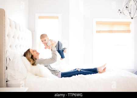 Vue de côté maman holding baby boy jusqu'au lit dans la chambre Banque D'Images