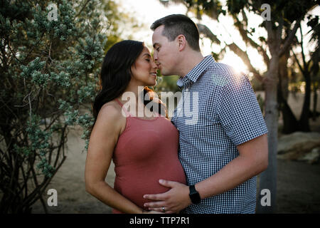 Mari kissing pregnant wife sur le nez alors qu'il se trouvait en stationnement pendant le coucher du soleil Banque D'Images