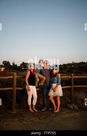 Portrait de famille heureuse par une clôture sur le terrain contre le ciel au coucher du soleil Banque D'Images