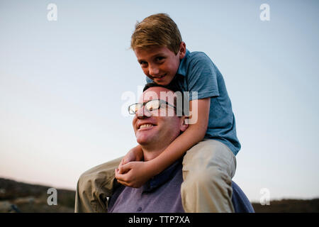 Smiling father carrying son on shoulders contre ciel clair pendant le coucher du soleil Banque D'Images