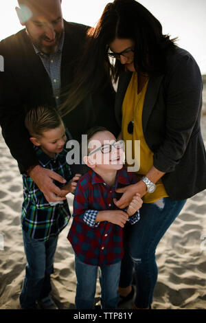 Heureux parents jouant avec fils en position debout au plage en journée ensoleillée Banque D'Images