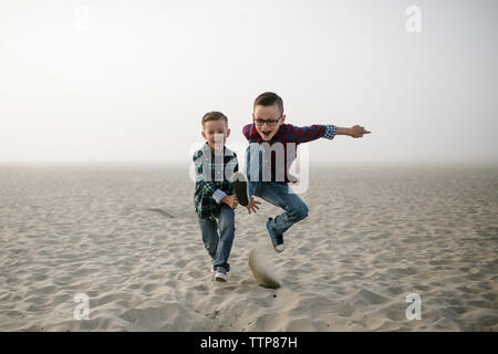 Les frères jumeaux sautant et jouant dans le sable sur Misty Day at the Beach Banque D'Images