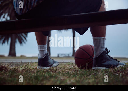 La section basse de l'homme assis sur un banc sur le terrain contre le ciel Banque D'Images