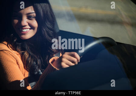 Portrait of happy woman driving car vu à travers le pare-brise Banque D'Images