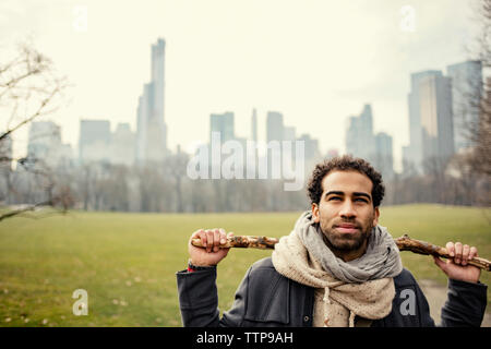 Jeune homme tenant un bâton et debout sur les champs contre cityscape Banque D'Images