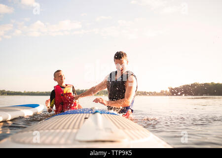 Père et fils bénéficiant au lac contre le ciel aux beaux jours Banque D'Images