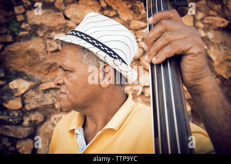 Close-up of man holding contrebasse debout contre un mur en pierre Banque D'Images