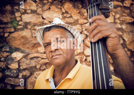 Portrait of man holding contrebasse debout contre un mur en pierre Banque D'Images