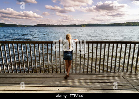 Vue arrière du Girl standing on jetty by railing sur le lac et à la vue de Banque D'Images