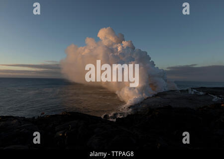 À partir de la fumée au volcan émettant plage contre le ciel au coucher du soleil Banque D'Images