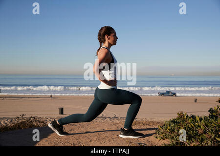 Vue de côté de femme avec les mains sur l'étirement de la hanche contre clear sky at beach Banque D'Images