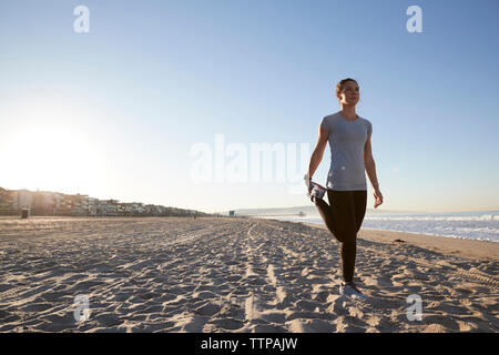 Toute la longueur du portrait tout en se tenant sur une jambe contre clear sky at beach Banque D'Images