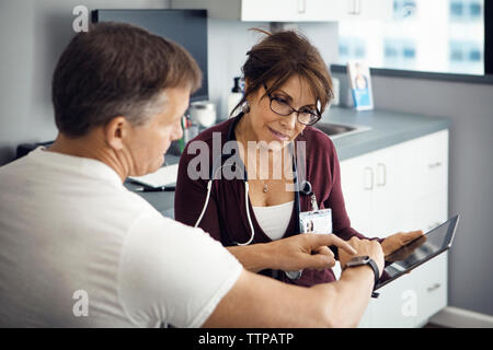 Patient de sexe masculin montre-bracelet au pointage tout en discutant avec femme médecin en clinique Banque D'Images