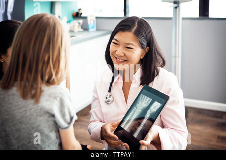 Smiling female doctor showing hand x-ray on tablet computer to girl in clinic Banque D'Images