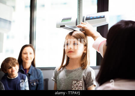 Mesurer la hauteur de la jeune fille médecin alors que family sitting in clinic Banque D'Images