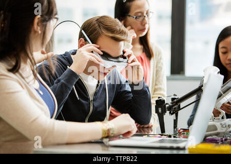 Male student portant des lunettes de réalité virtuelle, en position assise par des amis en classe Banque D'Images