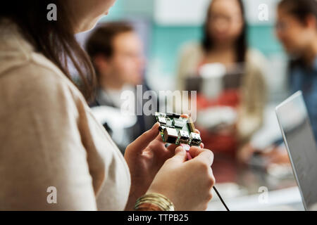 Portrait d'étudiant la carte de circuits imprimés, câbles de fixation avec des amis et des enseignants en arrière-plan Banque D'Images