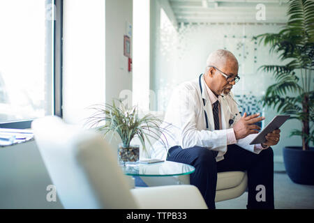 Doctor using tablet computer while sitting on sofa in hospital Banque D'Images