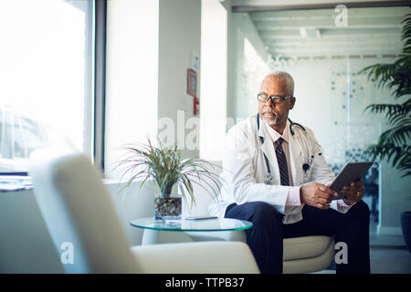 Médecin à l'écart tout en étant assis à l'ordinateur tablette sur canapé à l'hôpital Banque D'Images