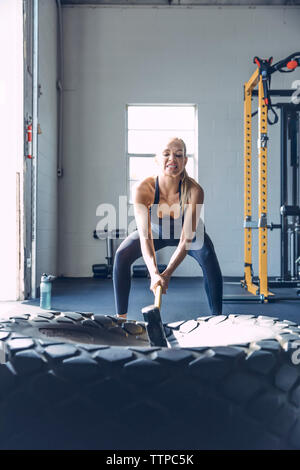 Femme déterminée de frapper le pneu avec marteau tout en exerçant en salle de sport Banque D'Images