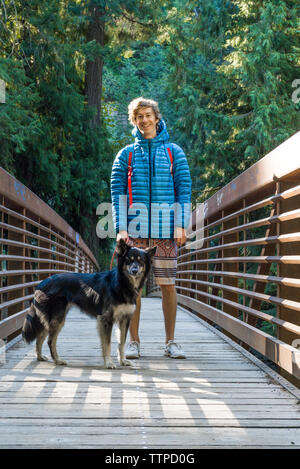 Portrait of happy man with dog standing on footbridge in forest Banque D'Images