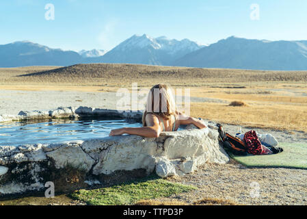 Vue arrière de femme assise en piscine sur terrain Banque D'Images